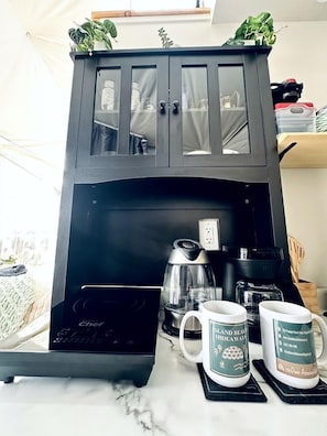 A kitchen area with a coffee maker, two mugs, and a cabinet with glass doors.