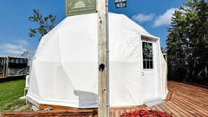 Ett vitt tält med dörr och fönster, en träveranda och en skylt med texten ”Tranquility Island Beach Hideaway”.