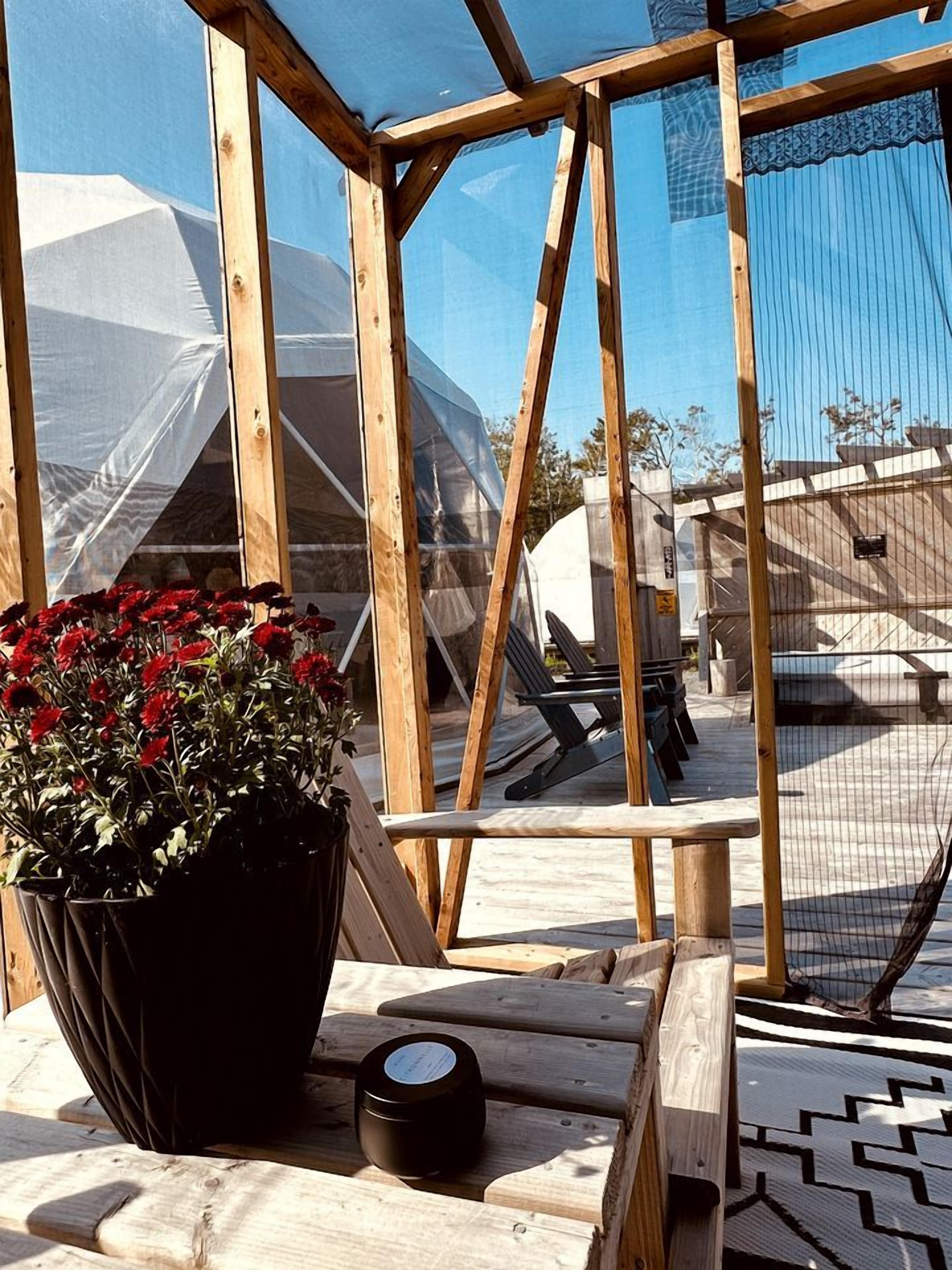 Eine Holzterrasse mit einem Blumentopf und einer Kerze, mit Blick auf einen Poolbereich mit Zeltdach.