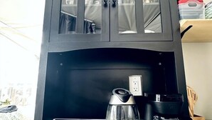 Ett köksutrymme med en kaffebryggare, två muggar och ett skåp med glasdörrar.