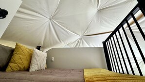 A bedroom with a sloped ceiling, a bed with a headboard, and a window with a black metal frame.