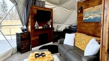 A tented living area with a sofa, a small table, a fireplace, and an air conditioning unit.