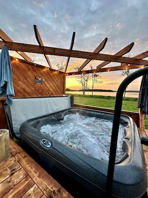 Un bain à remous avec une terrasse en bois et une vue sur un lac au coucher du soleil.