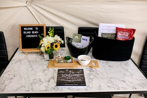 A marble table with a welcome sign, a guest book, a flower vase, a basket of snacks, and a thank you card.