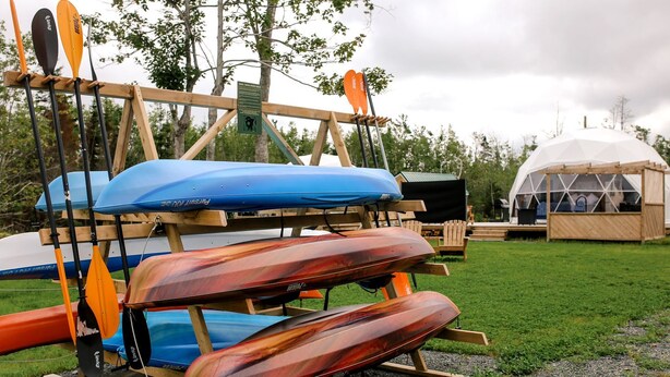 A row of canoes and paddles on a wooden rack, a white dome-shaped structure, and a wooden deck with chairs.