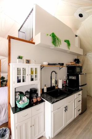 A compact kitchen with white cabinetry, a black countertop, and a microwave.