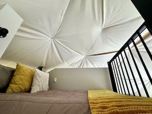 Une chambre avec un plafond en pente, un lit doté d’une tête de lit et une fenêtre avec un cadre en métal noir.