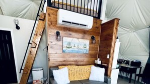 Un interior moderno con un sofá gris, paredes de madera, un tapete blanco y una escalera de madera.