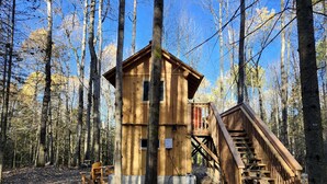 A wooden cabin with a staircase leading to a deck, surrounded by tall trees.
