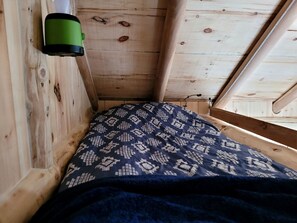 A small, cozy room with a wooden ceiling and walls, a patterned bedspread, and a green object on the wall.