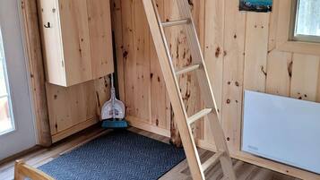 L’intérieur d’une cabane en bois, avec une échelle, un balai, une fenêtre et un tableau accroché au mur.
