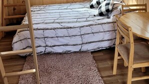 A wooden cabin room with a loft bed, a wooden table, and two windows.