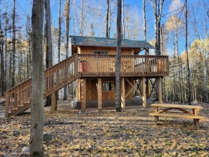 A wooden cabin with a balcony, a wooden deck, and a picnic table in a forest. - Unique Tree House Perfect for Families with BBQ in Callander, Ontario (Corbeil)