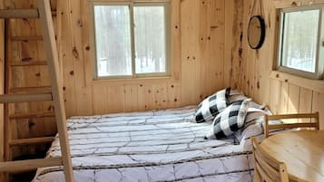 A wooden cabin room with a loft bed, a wooden table, and two windows.