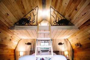 A wooden cabin interior with a bed, a ladder, and two fish mounted on the ceiling.