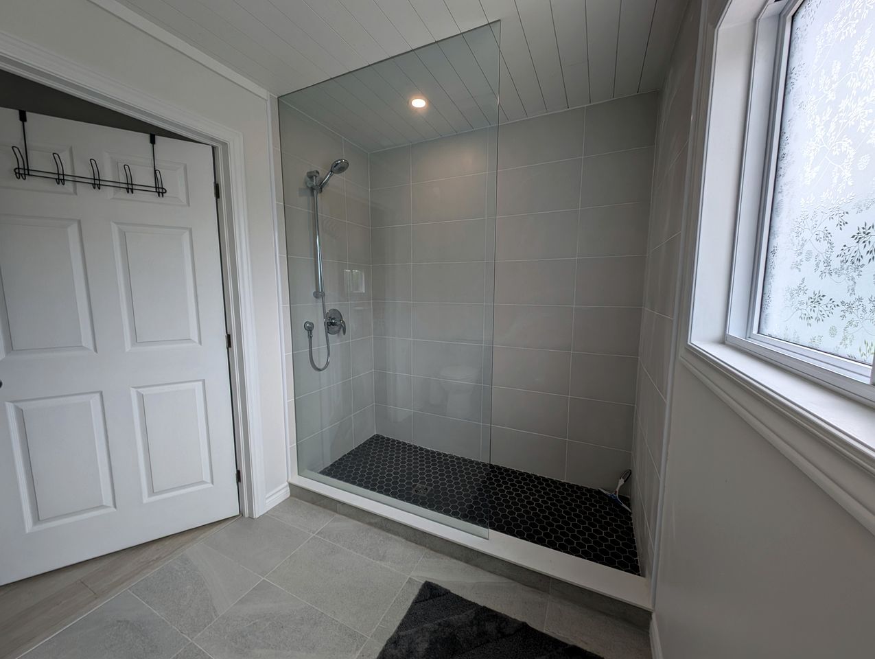 Ein modernes Badezimmer mit Duschabtrennung aus Glas, einer weißen Tür und einem Fenster.