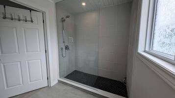 Ein modernes Badezimmer mit Duschabtrennung aus Glas, einer weißen Tür und einem Fenster.