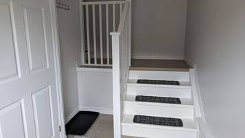 A staircase with white railings and steps, a black doormat, and a light-colored rug.