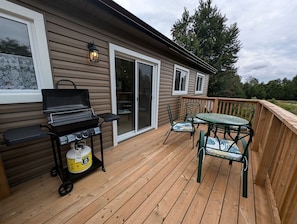 A wooden deck with a grill, chairs, and a table.