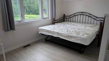 A room with a bed, a window with curtains, and a view of greenery outside.