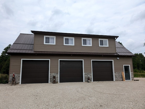 A two-story building with three large garage doors, a small entrance door, and a gravel driveway.