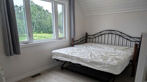 Une chambre avec un lit, une fenêtre avec des rideaux et une vue sur la verdure.