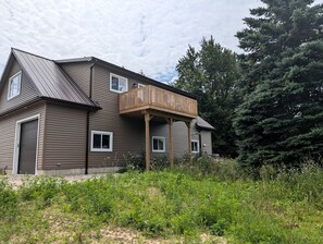 A two-story house with a balcony, a garage, and a wooded area in the background.