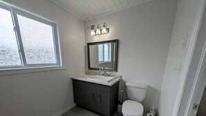 Une salle de bain avec des toilettes blanches, un meuble de couleur gris foncé, un lavabo blanc et une fenêtre en verre dépoli.