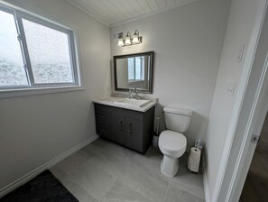 A bathroom with a white toilet, dark grey cabinet, white sink, and a window with frosted glass.