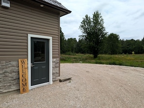 A building with a 'WELCOME' sign, a door, and a gravel driveway. - Aspen Acres Cabin with BBQ and Private Deck (Chatsworth)