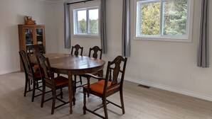 Une salle à manger avec une table et des chaises en bois, un buffet en bois et deux fenêtres avec des rideaux.