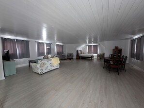 A spacious living room with a sofa, a dining table with chairs, a bed, and a TV.