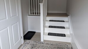 Un escalier avec des rampes et des marches blanches, un paillasson noir et un tapis de couleur claire.