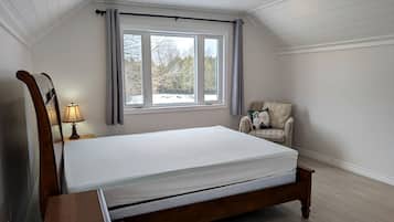 Een slaapkamer met een houten bed, een nachtkastje, een lamp, een raam met gordijnen en een stoel.
