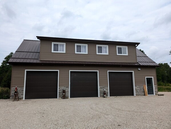 A two-story building with three large garage doors, a small entrance door, and a gravel driveway.