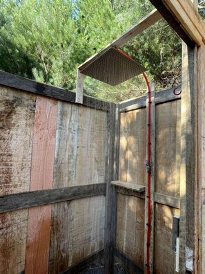 Un espace de douche extérieur en bois, doté d’un toit en bois et d’un tuyau rouge.