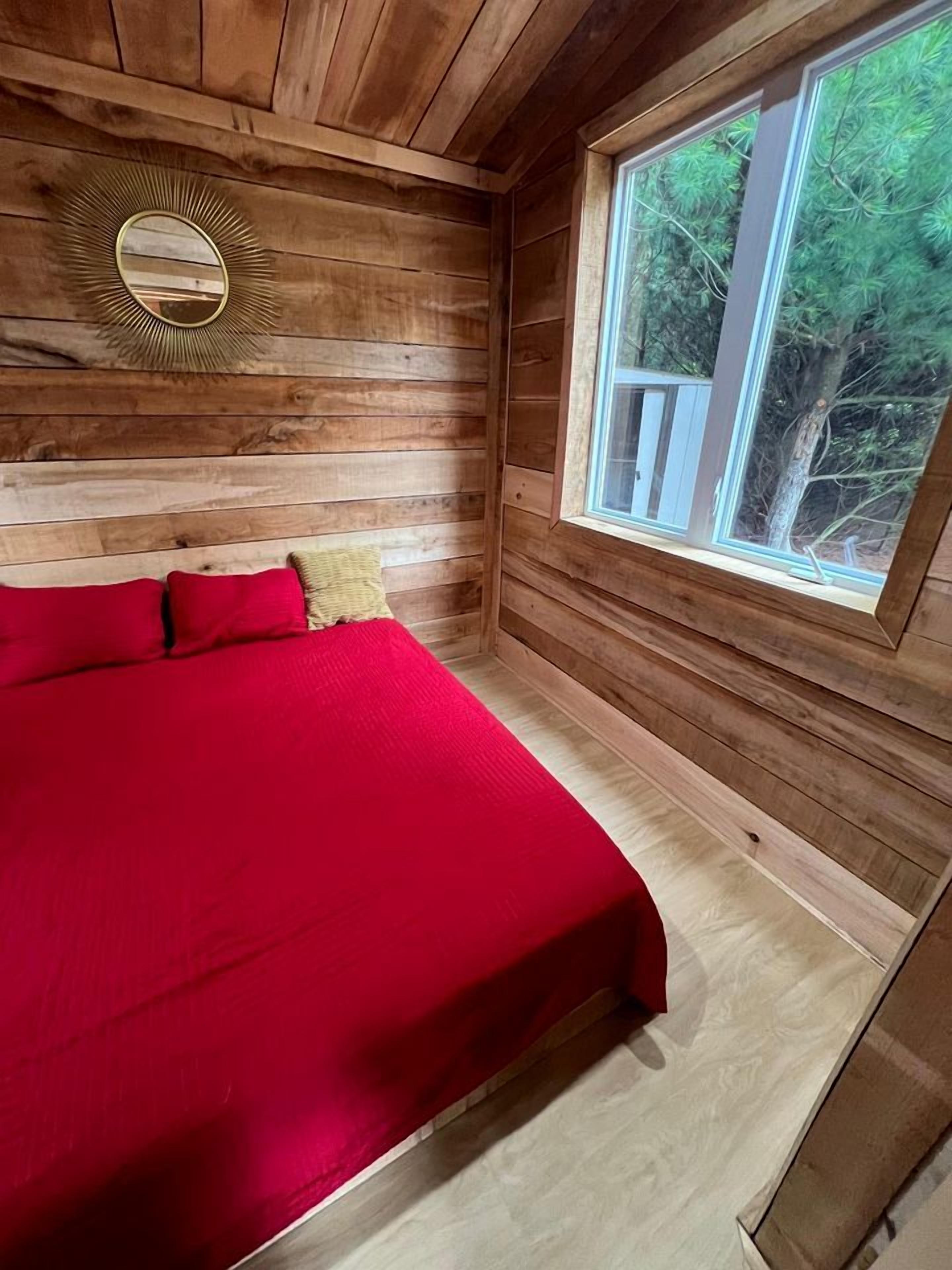 Ein Schlafzimmer einer Holzhütte mit Bett, Fenster und Spiegel.