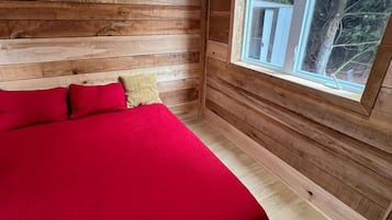 Ein Schlafzimmer einer Holzhütte mit Bett, Fenster und Spiegel.