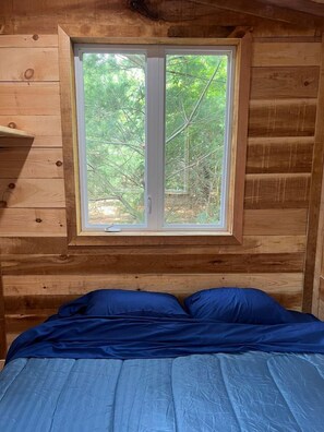 Ein Zimmer in einer Holzhütte mit Bett, Fenster und Ablagefläche.