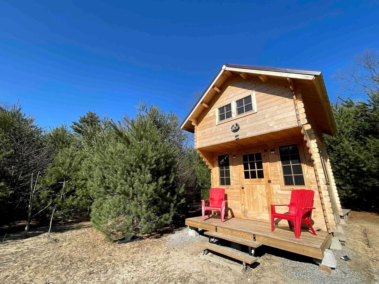 Une cabane en bois avec un porche, deux chaises rouges et un ciel dégagé.