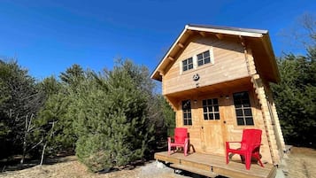 Une cabane en bois avec un porche, deux chaises rouges et un ciel dégagé.