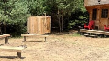 A cabin with a wooden deck, a covered seating area, and a large wooden structure.