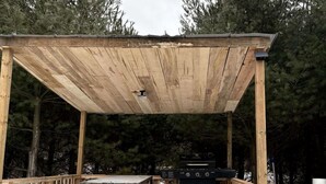 Eine Holzterrasse mit Picknicktisch und Grillplatz, umgeben von Bäumen.