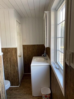 Une petite salle de bain avec un lavabo blanc, des toilettes et une fenêtre.