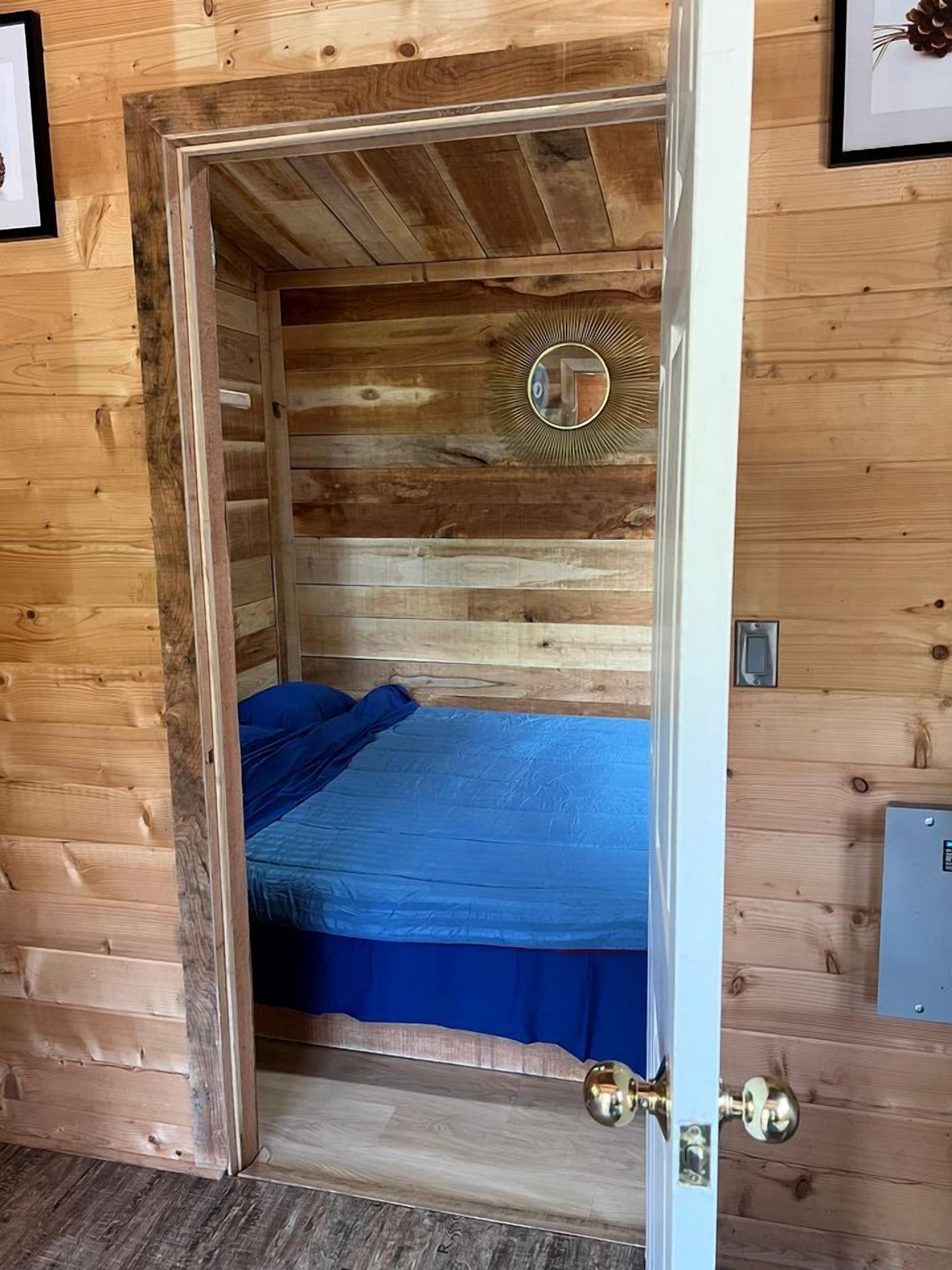 Ein Zimmer in einer Holzhütte mit einem Bett, einem Spiegel und einer Tür.