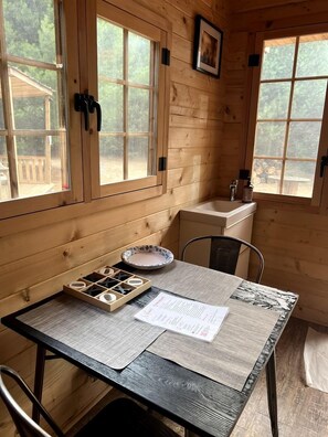 L’intérieur d’une cabane en bois, avec une table à manger, des chaises, un évier et des fenêtres.