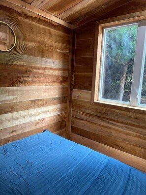 Una habitación de cabaña de madera con una cama, un ventanal y un espejo fijado a la pared.