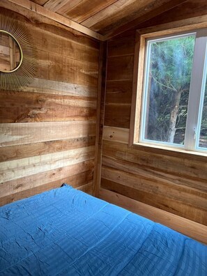 Een houten kamer met een bed, een raam en een spiegel aan de muur.