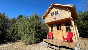 Eine Holzhütte mit Veranda, zwei roten Stühlen und blauem Himmel.