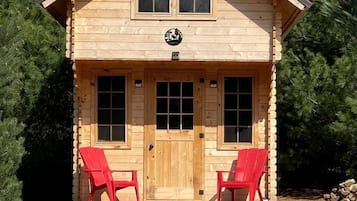Une cabane en bois avec un porche à l’avant, deux fenêtres et une porte.